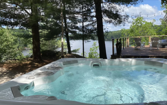 A hot tub on a wooden deck overlooking a treed lakeshore in summer