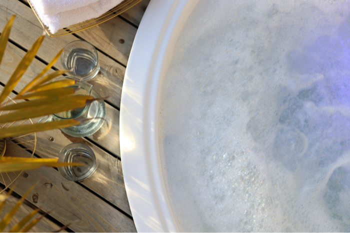 A bubbling hot tub on a wooden deck with glasses of water nearby