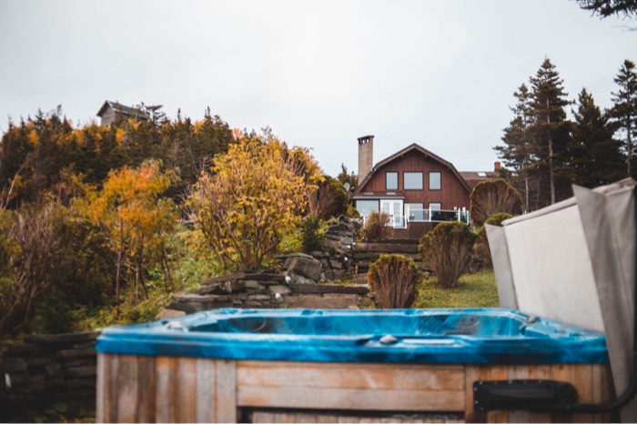 A backyard hot tub on a deck with autumn trees and a house behind
