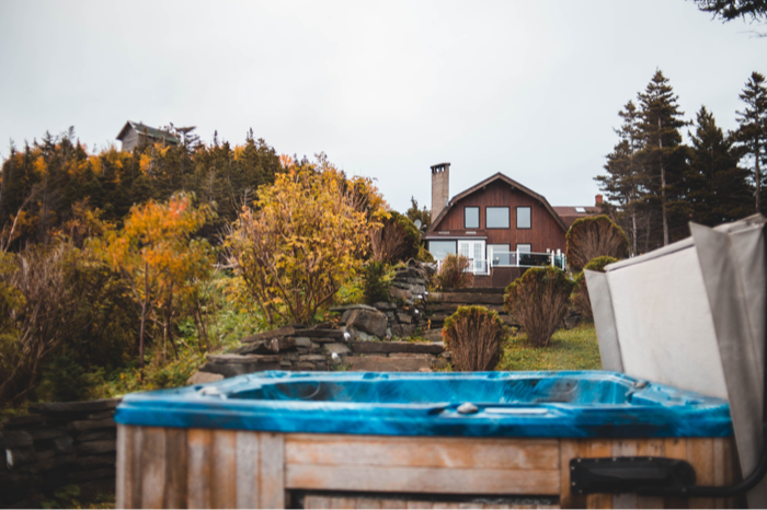 A backyard hot tub on a deck with autumn trees and a house behind