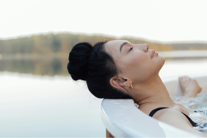 A woman resting her head back with eyes closed in a lakeside hot tub