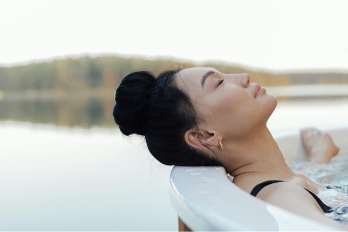 A woman resting her head back with eyes closed in a lakeside hot tub
