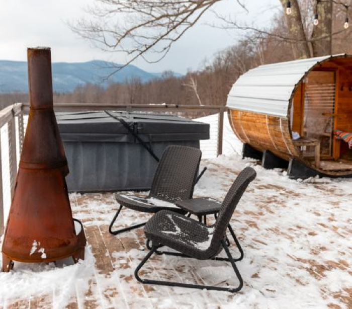 A barrel hot tub, chiminea heater, and chair in a snowy backyard