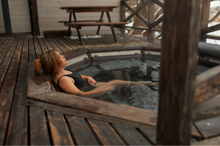 A woman relaxing in a wooden deck hot tub in winter