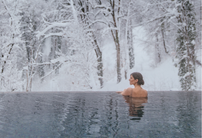 A person soaking in a hot tub overlooking a snowy winter forest