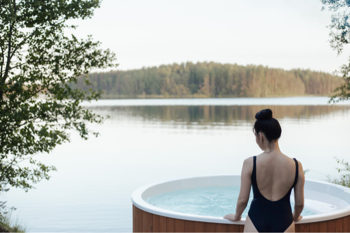 A woman standing in a wood-panelled hot tub looking out over a calm lake