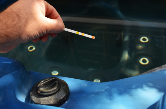 A hand dipping a test strip into a hot tub to check the water
